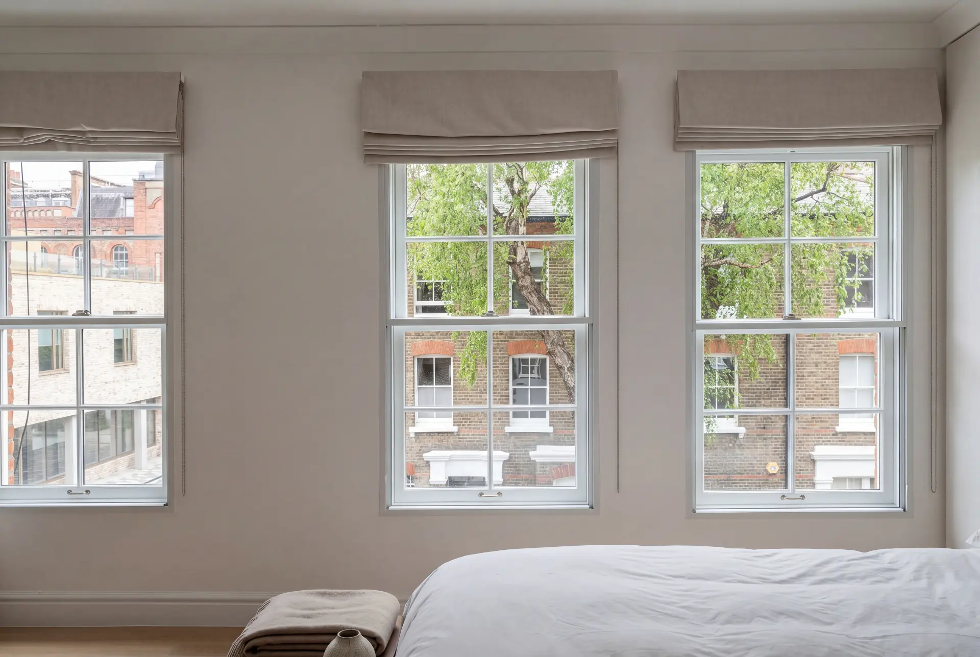 Triple sash bedroom — secondary glazing in Fitzrovia, London Bedroom with three secondary glazed sash windows and roman blinds facing a brick mews