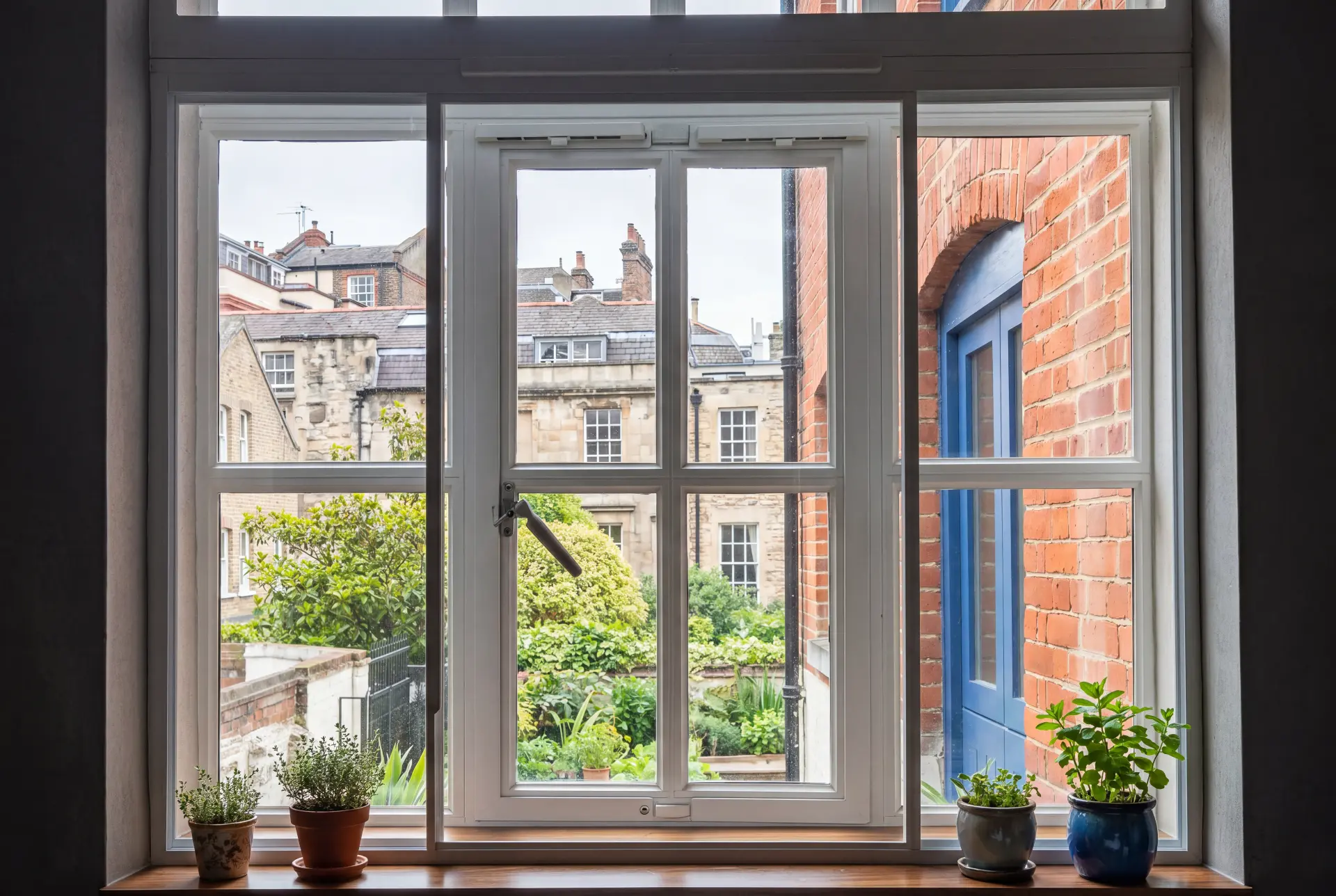 Garden view casement — secondary glazing in Stoke Newington, London Secondary glazed casement window with herb pots on the sill overlooking a walled London garden